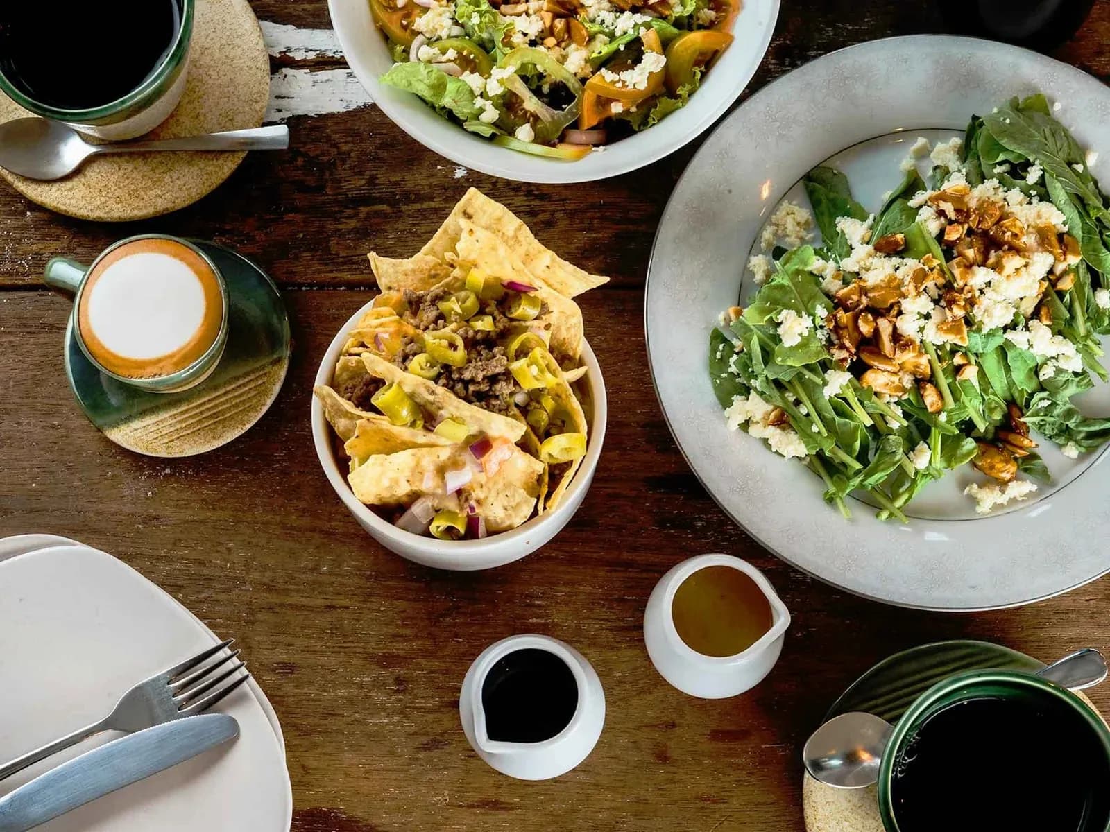 Cafe table spread with salads, nachos, coffee and dressings.