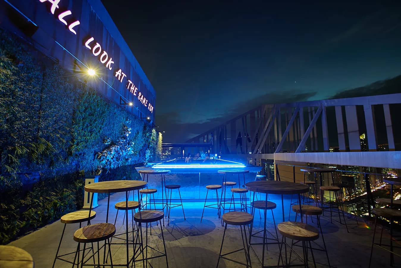 Blue-lit rooftop bar and high tables overlooking the city at night.